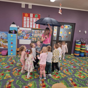 Dzieci są zdziwione różnym zastosowaniem parasola do zabaw w klasie. 